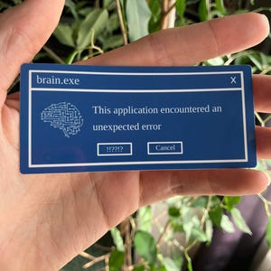 Peut inclure: Une carte rectangulaire bleue avec le texte "brain.exe" et un schéma de cerveau. La carte affiche un message d'erreur simulé : "This application encountered an unexpected error." Les boutons indiquent "!!??!?" et "Cancel."