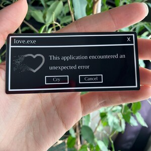 Könnte beinhalten: Eine schwarze rechteckige Karte mit weißem Text und Grafiken. Auf der Karte steht oben "love.exe", mit einer Grafik eines Herzens und dem Text "Diese Anwendung ist auf einen unerwarteten Fehler gestoßen." Darunter befinden sich die Schaltflächen "Cry" und "Cancel".