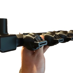 May include: A matte black plastic manifold component featuring a single vertical cylindrical intake port on one end and four horizontal, flattened nozzle outlets extending along the main rectangular body structure.