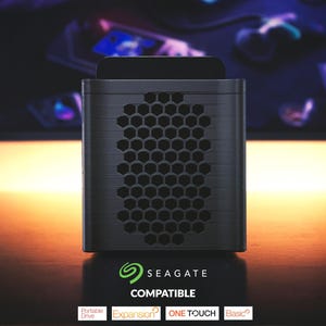 Könnte beinhalten: Eine schwarze und graue externe Festplatte mit einem Wabenmuster auf der Vorderseite. Die Festplatte hat das Seagate-Logo und das Wort "COMPATIBLE" darunter. Die Wörter "Portable Drive", "Expansion", "ONE TOUCH" und "Basic" sind ebenfalls sichtbar.