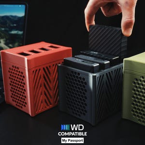 Op de afbeelding: Een afbeelding toont drie gekleurde externe harde schijfbehuizingen. Een hand plaatst een zwarte harde schijf in een zwarte behuizing. De behuizingen zijn rood, zwart en olijfgroen. De tekst "WD COMPATIBLE My Passport" staat onderaan.