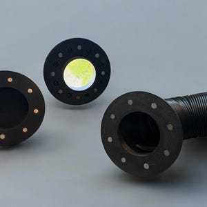 May include: Three black circular objects with evenly spaced holes and a corrugated black tube. The circular objects have a central hole, with one object having small, gold-colored dots around the center.