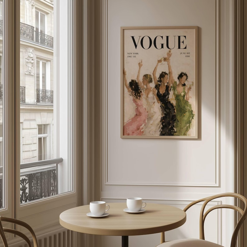 May include: A framed Vogue magazine cover print featuring a watercolor illustration of women in gowns. The print has the Vogue logo at the top and the text "New York, June 1st 1930". The print is displayed above a round wooden table with two white teacups.