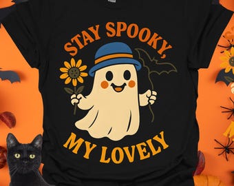 May include: Black t-shirt with a Halloween-themed graphic. The design features a cartoon ghost wearing a blue hat and holding a sunflower and a bat. The text "Stay Spooky, My Lovely" is in orange.