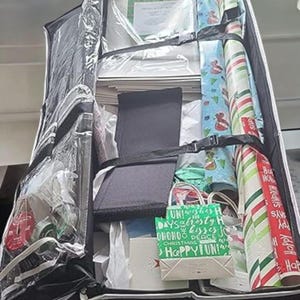 May include: A black and clear storage bag filled with gift wrapping supplies. Rolls of wrapping paper in various festive designs, including red and white stripes and blue with holiday motifs. Gift bags and boxes are also visible.