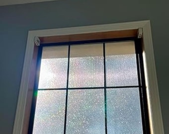 May include: A window with a grid design, featuring a light-coloured roller blind at the top. The window frame is dark, and the glass has a textured, frosted appearance. The surrounding wall is painted a light grey.