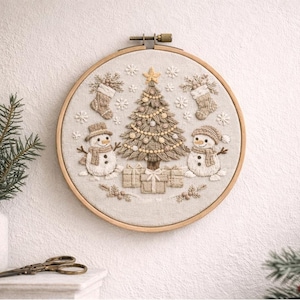May include: Embroidered Christmas scene in a wooden hoop. The design features a decorated Christmas tree, two snowmen, stockings, gifts, and snowflakes. The color palette includes beige, brown, and gold tones, creating a festive holiday decoration.
