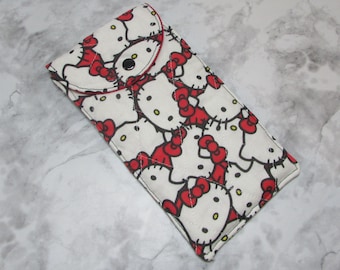 May include: A rectangular glasses case featuring a repeating pattern of Hello Kitty faces with red bows on a white background. The case has a black snap closure and a red trim. The case is made of a quilted fabric.