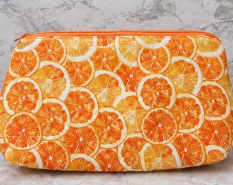 May include: A zippered cosmetic bag featuring a vibrant pattern of orange slices in shades of orange and white. The bag has a curved shape and a matching orange zipper. The bag is a bright and cheerful accessory.