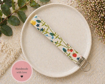 Llavero de muñeca de algodón con estampado floral color crema, correa de tela para llavero, herrajes plateados.