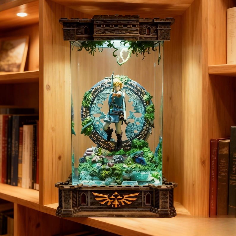 Puede incluir: Una vitrina detallada con una figura de un personaje con t&uacute;nica azul, de pie frente a un emblema circular. La vitrina tiene una base y una parte superior de madera, con una carcasa de vidrio. El emblema est&aacute; rodeado de follaje verde.