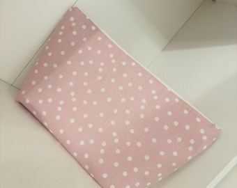 May include: A pink polka dot pouch with white dots. The pouch is made of fabric and has a white interior. The pouch is resting inside a white shelf.