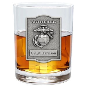 May include: A clear glass tumbler filled with amber liquid and ice cubes. A silver-colored plaque with the word "MARINES" and a military emblem is affixed to the glass. The name "GySgt Harrison" is below the emblem.