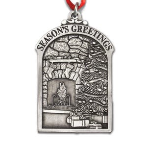 May include: A silver-toned metal ornament shaped like an archway with a red ribbon loop at the top. The embossed design features a stone fireplace with stockings, a decorated Christmas tree, and wrapped gifts, with the text SEASON'S GREETINGS.