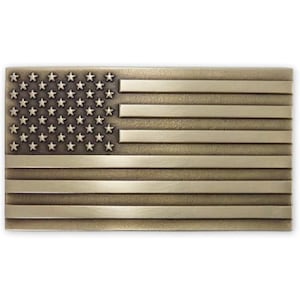 May include: A rectangular metal belt buckle with a design of the American flag. The buckle features a bronze finish with stars in the upper left corner and horizontal stripes. The stars and stripes are slightly raised.