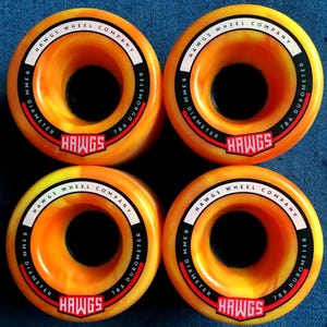 May include: Four orange and yellow skateboard wheels with the text "HAWGS WHEEL COMPANY" and "63mm DIAMETER 78A DUROMETER" printed on the side. The wheels have a black center.