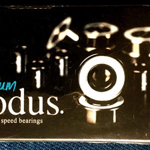 May include: A black box with the words "Titanium Modus" in white and teal lettering. The words "speed bearings" are below the main text. Several silver bearings are visible in the background.