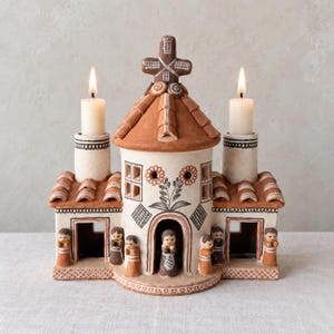 May include: A terracotta candle holder shaped like a building with a central dome, two side towers, and a cross on top. The structure features painted floral motifs, geometric patterns, and small human figures standing in front of the doorways.
