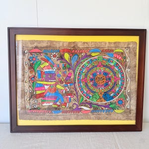 May include: A framed painting on textured brown paper featuring a purple deity figure on the left and a colorful circular Aztec calendar design on the right. The artwork includes vibrant floral motifs, intricate patterns, and the word MARZO.