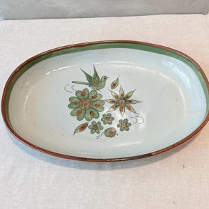 May include: An oval ceramic serving platter with a light blue interior and a brown rim. The center features a hand-painted design of a green bird perched above a cluster of green and orange flowers and leaves, with a thin green band along the edge.