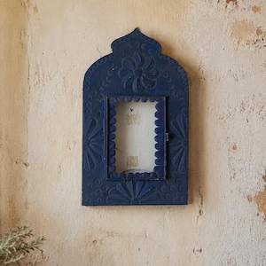 May include: A dark blue rectangular wall mirror with an arched top and a scalloped inner frame. The wooden frame features carved floral and fan-shaped motifs across its surface. The central glass pane is clear and rectangular in shape.