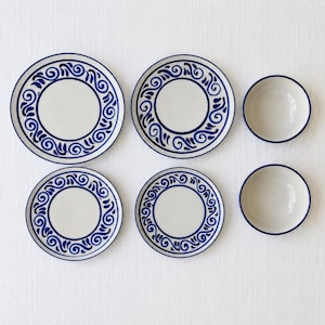May include: A set of six ceramic dishes consisting of two large plates, two smaller plates, and two bowls. Each piece features a cream-colored base with a dark blue decorative border pattern of swirling lines and leaf-like shapes around the rim.