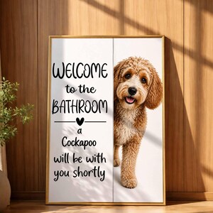 May include: Framed wall art with a gold border. The artwork features a Cockapoo dog peeking out from behind a white panel. Text reads "WELCOME to the BATHROOM a Cockapoo will be with you shortly."