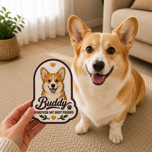 May include: A smiling Pembroke Welsh Corgi dog with tan and white fur sits next to a patch. The patch has a portrait of a Corgi, the name "Buddy", and the text "FOREVER MY BEST FRIEND". The patch is brown and cream colored.
