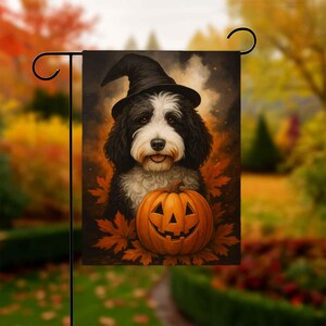 以下が含まれることがあります： ハロウィーンのガーデンフラッグ。黒と白の犬が魔女の帽子をかぶり、彫刻されたカボチャと秋の葉があります。犬はフレンドリーな表情をしています。背景はぼやけた秋のシーンです。