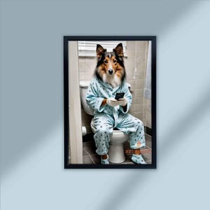 May include: Framed print featuring a dog dressed in a light blue robe and pajamas, sitting on a toilet while holding a smartphone. The dog has brown, black, and white fur. The print is in a black frame and is against a light blue wall.