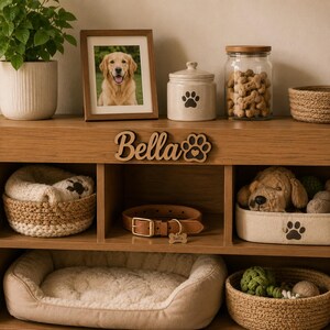 Pu&ograve; includere: Un mobiletto in legno per animali domestici con il nome Bella e un'impronta di zampa intagliata. L'unit&agrave; include un collare in pelle marrone con medaglietta in metallo, una cuccia color crema, cesti intrecciati, un barattolo in ceramica e una foto.