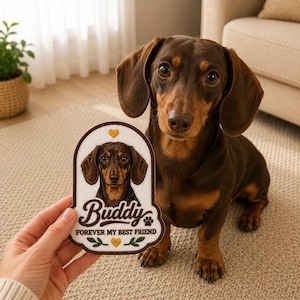May include: A brown and tan dachshund dog sits next to a patch with a portrait of a dachshund. The patch has the name "Buddy" and the text "Forever My Best Friend". The patch has a white background with a brown border and yellow heart accents.