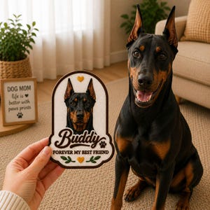 May include: A black and tan Doberman Pinscher sits next to a decorative patch. The patch features a Doberman portrait, the name "Buddy", and the phrase "FOREVER MY BEST FRIEND". A small framed sign reads "DOG MOM life is better with paws prints".