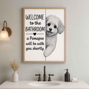 Pode incluir: Placa de casa de banho emoldurada com uma ilustração de um cão Pomapoo. A placa diz "WELCOME to the BATHROOM" e "a Pomapoo will be with you shortly". A obra de arte é em preto e branco, emoldurada em madeira clara.