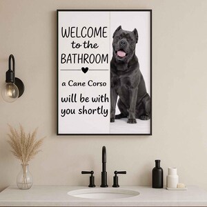 May include: Framed bathroom wall art with a Cane Corso dog. The artwork has the text "WELCOME to the BATHROOM" above a heart symbol, followed by "a Cane Corso will be with you shortly". The dog is a dark grey colour.