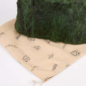 May include: A dark green, textured bag rests on a tan drawstring bag. The dark green bag has a plush, fur-like appearance. The tan bag is printed with black text and logos, and has a drawstring closure.