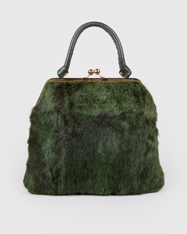 May include: A vintage handbag with a green fur exterior and a matching green leather handle. The bag features a gold-toned clasp and a structured rectangular shape, offering a classic and elegant design. The bag's dimensions are approximately 10 inches wide and 8 inches tall.