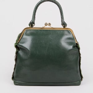 May include: A dark green handbag with a structured frame and a top handle. The bag features a gold-colored clasp and trim, with fur accents on the sides. The bag's design is reminiscent of vintage styles.
