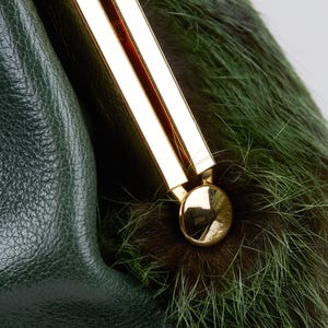 May include: Close-up of a green leather handbag with a gold-colored clasp. The bag features a section of green and brown fur. The leather has a textured appearance, and the clasp is a shiny gold color.