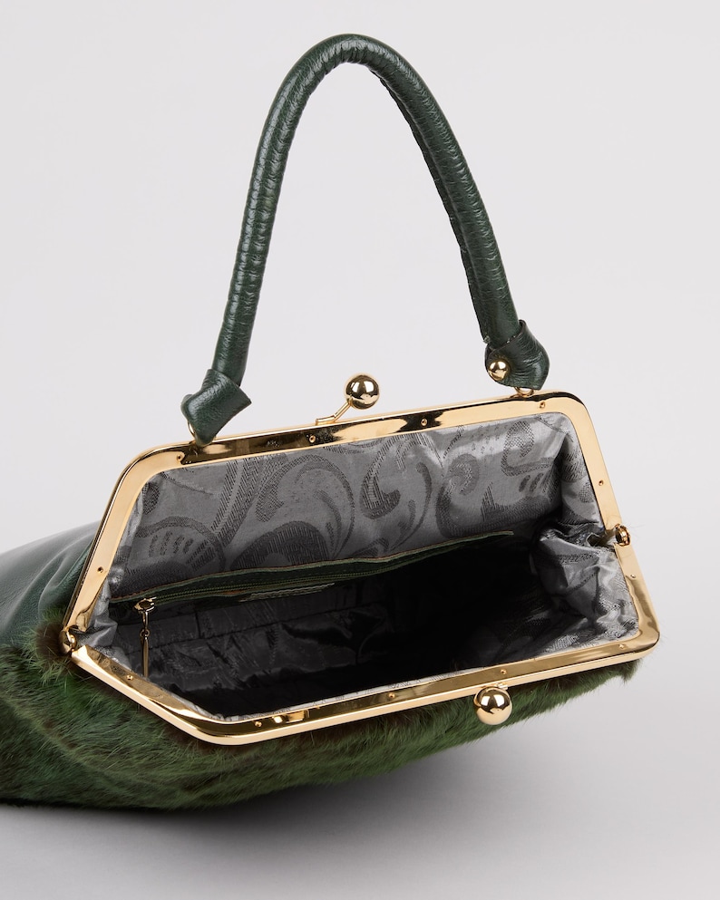 May include: A green handbag with a gold-colored frame and a matching handle. The bag's exterior has a textured, fur-like appearance. The interior is lined with a patterned fabric. The bag is open, revealing the inside.