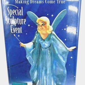 May include: A fairy figurine with blonde hair, blue wings, and a blue dress, holding a wand. The figurine is on a base with the text "Special Sculpture Event" and "Making Dreams Come True". The base has the text "Classics Disney Collection".