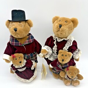 Puede incluir: Cuatro osos de peluche marrones vestidos con trajes de terciopelo burdeos y cuadros. Un oso lleva un sombrero de copa negro y gafas. Los otros osos visten vestidos con adornos de encaje. Cada oso sostiene un oso más pequeño, creando un tema familiar.