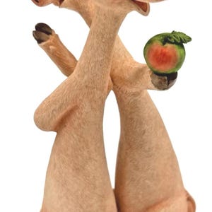 May include: A charming figurine depicting two pigs in an embrace. The pigs are a pale pink colour with detailed features, including closed eyes and a small watermelon. The figurine is set against a white background, highlighting the playful design.