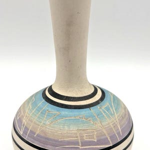 Könnte beinhalten: Eine Keramikvase mit cremefarbenem Hals und rundem Körper. Der Körper weist ein Design mit blauen, lila und cremefarbenen Farben auf, das durch schwarze Streifen akzentuiert wird. Die Vase hat eine einzigartige Form und dekorative Ausstrahlung.