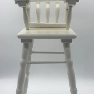May include: A white wooden high chair with a backrest featuring the "Cabbage Patch Kids" logo. The chair has a square seat, four spindles, and four legs. The chair is painted white and appears to be vintage.