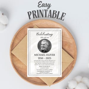 May include: A printable memorial card with the text "Celebrating the Life of Michael Oliver 1950-2025." The card features a black and white photo of a man and is set on a wooden plate with a brown envelope.