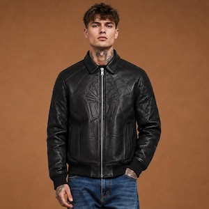 May include: A black leather jacket with a full-length silver zipper, a pointed collar, and ribbed cuffs, paired with blue denim jeans and black leather shoes. The jacket features a subtle geometric panel design on the chest and sleeves.