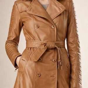 May include: A tan leather trench coat with a double-breasted design, featuring a belted waist and decorative stitching on the sleeves. The coat has a classic collar and button closures, offering a timeless style.