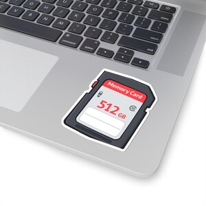 Peut inclure: Un autocollant de carte mémoire noire et rouge avec le texte "Memory Card" et "512 Go". L'autocollant est sur un ordinateur portable argenté.