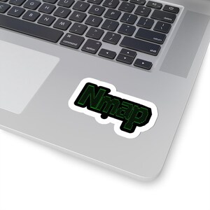 May include: A white sticker with the word "Nmap" in green, pixelated font, outlined in black. The sticker is placed on a silver laptop, with the keyboard visible.